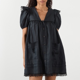 Model wearing Ganni black linen mini dress with puff sleeves, V-neck, button front, patch pockets and lace trim detailing.
