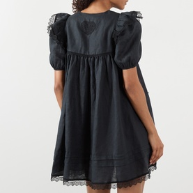 Model wearing Ganni black linen mini dress with puff sleeves, lace trim detailing and gathered skirt, shown from the back.