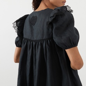 Model wearing Ganni black linen dress, back view showing puff sleeves, ruffle trim, lace detail, and smocked waist