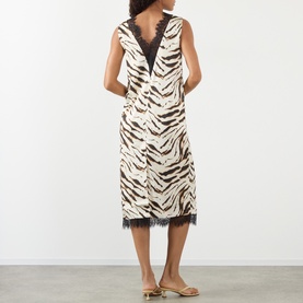 Model wearing Ganni Zebra Print Lace-Trim Slip Dress in Egret, showing V-back, black lace trim and midi length. Styled with tan sandals.