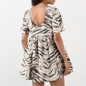 Model wearing Ganni dress in Egret tiger print, featuring a scoop back, puff sleeves, and full gathered skirt in 100% cotton.