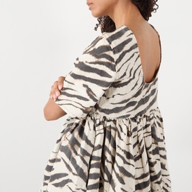 Model wearing Ganni Dress in Egret zebra print cotton, showing open back detail with gathered skirt silhouette