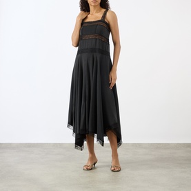 Model wearing Ganni black silk blend midi dress with lace trim detail and handkerchief hem, styled with gold flat sandals