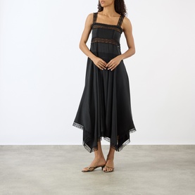 Model wearing Ganni black silk blend midi dress with lace trim inserts, handkerchief hem, and square neckline with tan sandals