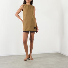 Model wearing Ganni Logo Patch Lace-Trim Mini Shift Dress in Ermine, sleeveless with black lace hem and heart logo patch, styled with strappy sandals.