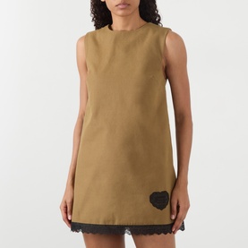Model wearing Ganni Logo Patch Lace-Trim Mini Shift Dress in Ermine, sleeveless with lace hem trim and heart logo patch at hip.