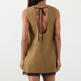 Model wearing Ganni Logo Patch Lace-Trim Mini Shift Dress in Ermine, showing U-shaped open back with black self-tie fastening and lace hem trim.