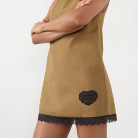 Model wearing Ganni Logo Patch Lace-Trim Mini Shift Dress in Ermine, showing lace hem detail and embroidered heart logo patch.