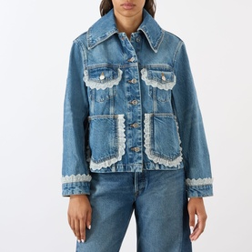 Model wearing Ganni Lace-Trim Denim Jacket in dark blue with white lace detailing, chest flap pockets and patch pockets, styled with blue jeans.