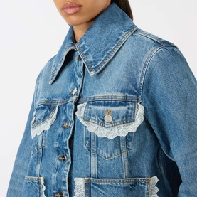 Model wearing Ganni Lace-Trim Denim Jacket in dark blue with enlarged collar, front button fastening and white lace-trim detailing on chest pockets.