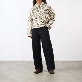 Model wearing Ganni Zebra Print Laminated Denim Jacket in Egret, styled with wide-leg black jeans and brown boots.