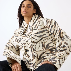 Model wearing Ganni Zebra Print Laminated Denim Jacket in Egret, featuring wide sleeves, point collar, and cropped length, styled with dark jeans.