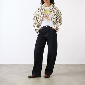 Model wearing Ganni Zebra Print Laminated Denim Jacket in Egret, styled with a graphic tee and wide-leg black jeans.