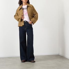 Model wearing Ganni Lari Wide-Leg Jeans in Rinse, dark wash rigid denim with tobacco stitching, styled with a tan jacket and graphic tee.