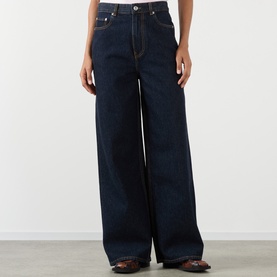 Model wearing Ganni Lari Wide-Leg Jeans in Rinse, high-rise dark wash denim with wide leg, tobacco stitching, styled with brown leather shoes.