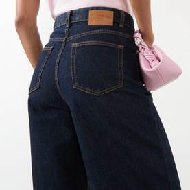 Model wearing Ganni Lari Wide-Leg Jeans in Rinse, high-rise dark wash denim with tobacco stitching, styled with a pink mini bag.