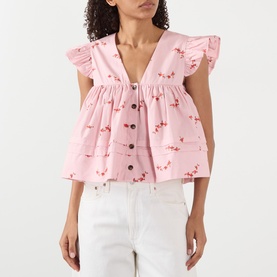 Model wearing Ganni pink floral cotton blouse with ruffle sleeves, V-neck and button front, styled with white jeans.