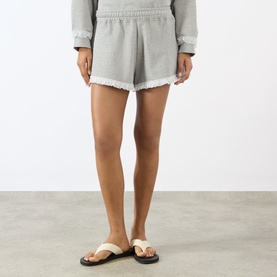 Model wearing Ganni Paloma cotton shorts with frayed hem, styled with matching grey sweatshirt and white strap sandals