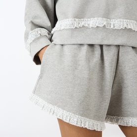 Model wearing Ganni Paloma grey marl cotton shorts with lace frill trim hem, styled with matching cropped sweatshirt