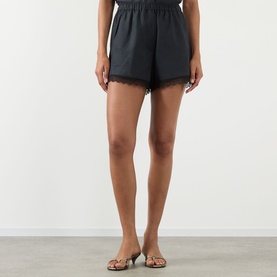 Model wearing Ganni black linen shorts with lace trim hem and elasticated waist, styled with strappy heeled sandals