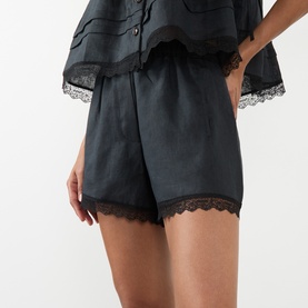 Model wearing Ganni black linen shorts with lace trim hem, styled with matching black lace-trim top
