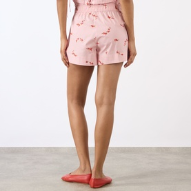 Model wearing Ganni pink cotton shorts with all-over flamingo print, elasticated waist. Styled with red flat shoes.