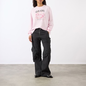 Model wearing Ganni Chalk Pink cotton sweatshirt with crab graphic, styled with dark grey wide-leg cargo trousers and black patent shoes.