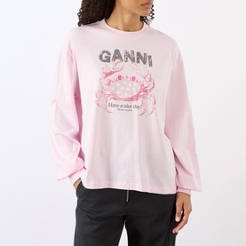 Model wearing Ganni Chalk Pink cotton long-sleeve sweatshirt with crab graphic print and "Have a nice day" slogan, paired with dark trousers.