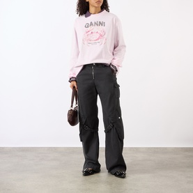 Model wearing Ganni Chalk Pink cotton sweatshirt with crab graphic, styled with dark cargo trousers, black heeled boots and small brown bag.