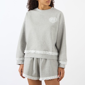Model wearing Ganni Isoli Logo Lace-Trim Sweatshirt in Paloma grey with lace-trim hem, styled with matching shorts
