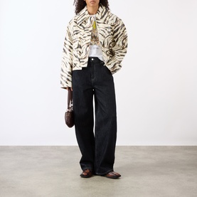Model wearing Ganni Tiger Logo Baby Tee in Bright White, styled with zebra-print jacket, black wide-leg jeans and brown loafers