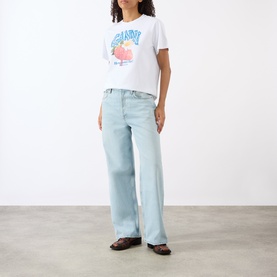 Model wearing Ganni Strawberry Logo T-Shirt in Bright White with light wash wide-leg jeans and dark brown loafers.