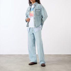 Model wearing Ganni Strawberry Logo T-Shirt in Bright White, styled with light blue denim jacket, wide-leg jeans, and brown loafers.