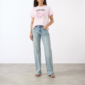 Model wearing Ganni Crab Logo T-Shirt in Chalk Pink with light-wash wide-leg jeans and tan strappy flat sandals.