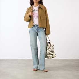 Model wearing Ganni Crab Logo T-Shirt in Chalk Pink with tan cropped jacket, light wash flared jeans, and zebra-print tote bag.