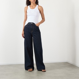 Model wearing Ganni Bright White cotton tank top, styled with dark indigo wide-leg jeans and black strappy sandals.