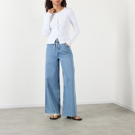 Model wearing Ganni Bright White cotton top with ruched front detail, styled with light blue wide-leg jeans and strappy sandals.