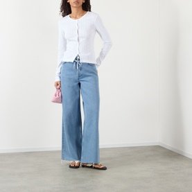 Model wearing Ganni Bright White cotton ribbed top with drawstring detail, styled with wide-leg jeans, pink mini bag and sandals