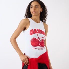 Model wearing Ganni Cherry Logo Ribbed Tank Top in Bright White with red cherry graphic, styled with red trousers tied at waist.
