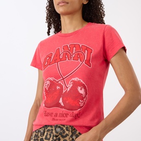 Model wearing Ganni Cherry Logo Baby Tee in High Risk Red with crew neck, short sleeves, and cherry graphic print. Styled with leopard print trousers.