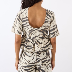 Model wearing Ganni Zebra Print Denim Flounce Top in Egret, low scoop back, flounce hem, styled with matching zebra print trousers.