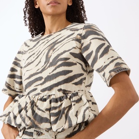 Model wearing Ganni Zebra Print Denim Flounce Top in Egret, featuring short sleeves, round neck and flounce hem detail.