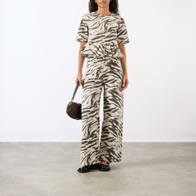 Model wearing Ganni Zebra Print Denim Flounce Top in Egret with matching wide-leg trousers, styled with a brown bag and black sandals.