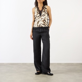 Model wearing Ganni Zebra Print Lace-Trim Blouse in Egret with black wide-leg trousers and black flat shoes.