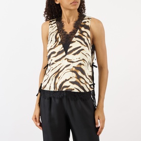 Model wearing Ganni Zebra Print Lace-Trim Blouse in Egret, sleeveless with V-neck lace trim and side-tie fastenings, styled with black trousers.