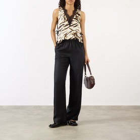 Model wearing Ganni Zebra Print Lace-Trim Blouse in Egret, styled with black wide-leg trousers, loafers and a small brown shoulder bag.
