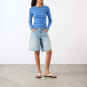 Model wearing Ganni Butterfly Logo Striped Long-Sleeved Top in Nouveau Navy, styled with light-wash denim shorts and flip-flop sandals.