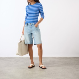 Model wearing Ganni Butterfly Logo Striped Long-Sleeved Top in Nouvean Navy, styled with light-wash denim shorts, sandals, and a canvas tote bag.