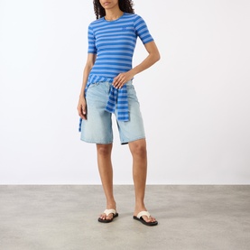 Model wearing Ganni Butterfly Logo Striped T-Shirt in Nouvean Navy with light-wash denim shorts and brown strappy flat sandals.