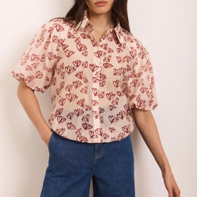 Model wearing Mint Velvet Heart Puff-Sleeve Shirt in pink with red heart print, classic collar and short puff sleeves, styled with blue jeans
